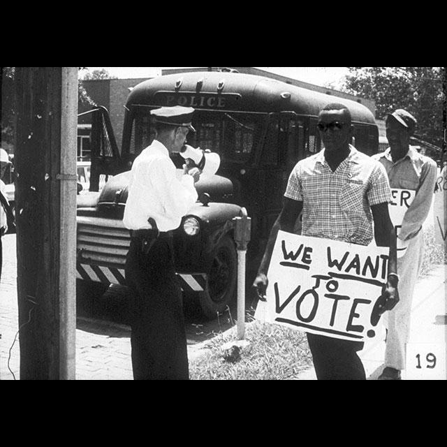 A black and white photograph of demonstrators holding protest signs